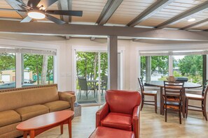 Ein modernes Interieur mit einer Couch, einem roten Sessel, einem Esstisch mit Stühlen und großen Fenstern mit Blick ins Freie.