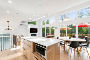 Eine moderne Küche mit Einbauofen, eine Essecke mit rundem Tisch und Stühlen sowie ein an der Wand montierter Fernseher.
