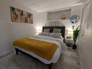 Ein Schlafzimmer mit einem Bett, Nachttischen, einem Spiegel, einem Fenster mit Jalousien und Wandbildern.