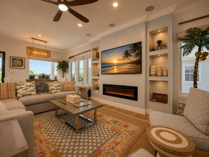 A living room with a sofa, coffee table, fireplace, and a large painting of a beach scene. - SE907 4BD, 4.5BA, Private Heated Pool, Pickleball Court, Parking for 5 (Port Aransas)