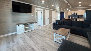 Ett rymligt vardagsrum med en platt-TV, en soffa, ett soffbord och ett kök i bakgrunden.