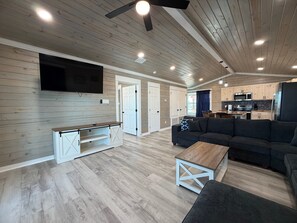 A spacious living area with a flat-screen TV, a sofa, a coffee table, and a kitchen in the background. - CL9 Shared Pool, Charcoal Grill, Old Town Port A (Port Aransas)