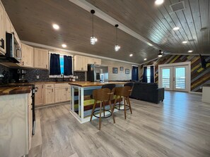 A modern kitchen with wooden cabinets, a central island, and bar stools. - CL9 Shared Pool, Charcoal Grill, Old Town Port A (Port Aransas)