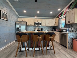 Eine moderne Küche mit Holzausbau, einem Edelstahlkühlschrank, einer Mikrowelle und einer Bar mit Hockern.