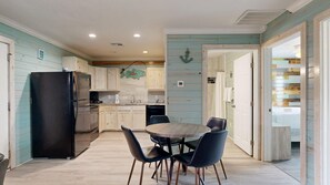 A compact kitchen with wooden cabinets, a black refrigerator, and a dining area with a round table and chairs. - ACC3 Shared Pool, In Town, Pet Friendly (Port Aransas)