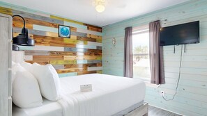 A bedroom with a bed, a wall-mounted TV, and a window with curtains. - ACC3 Shared Pool, In Town, Pet Friendly (Port Aransas)