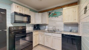 A kitchen with a stove, microwave, sink, and wooden cabinets. - ACC3 Shared Pool, In Town, Pet Friendly (Port Aransas)
