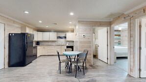 A modern kitchen with a black refrigerator, wooden cabinets, a dining table with chairs, and a visible bathroom door. - ACC5 Shared Pool, In Town, Pet Friendly (Port Aransas)