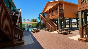 Um pátio com estruturas de madeira, piscina e mesas de piquenique.