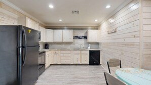 A kitchen with wooden cabinets, a black refrigerator, a coffee maker, and a tiled backsplash. - ACC5 Shared Pool, In Town, Pet Friendly (Port Aransas)