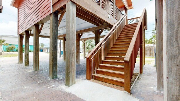 Un escalier en bois mène à un espace extérieur abrité, dont le sol est recouvert de briques.