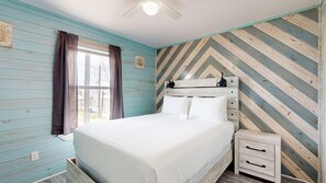 Ein Schlafzimmer mit einem Bett, einem Nachttisch, einer Kommode, einem Deckenventilator und einem Fenster mit Vorhängen.