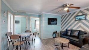 Une pièce comprenant une table à manger, des chaises, un canapé, un ventilateur de plafond et un téléviseur fixé au mur.
