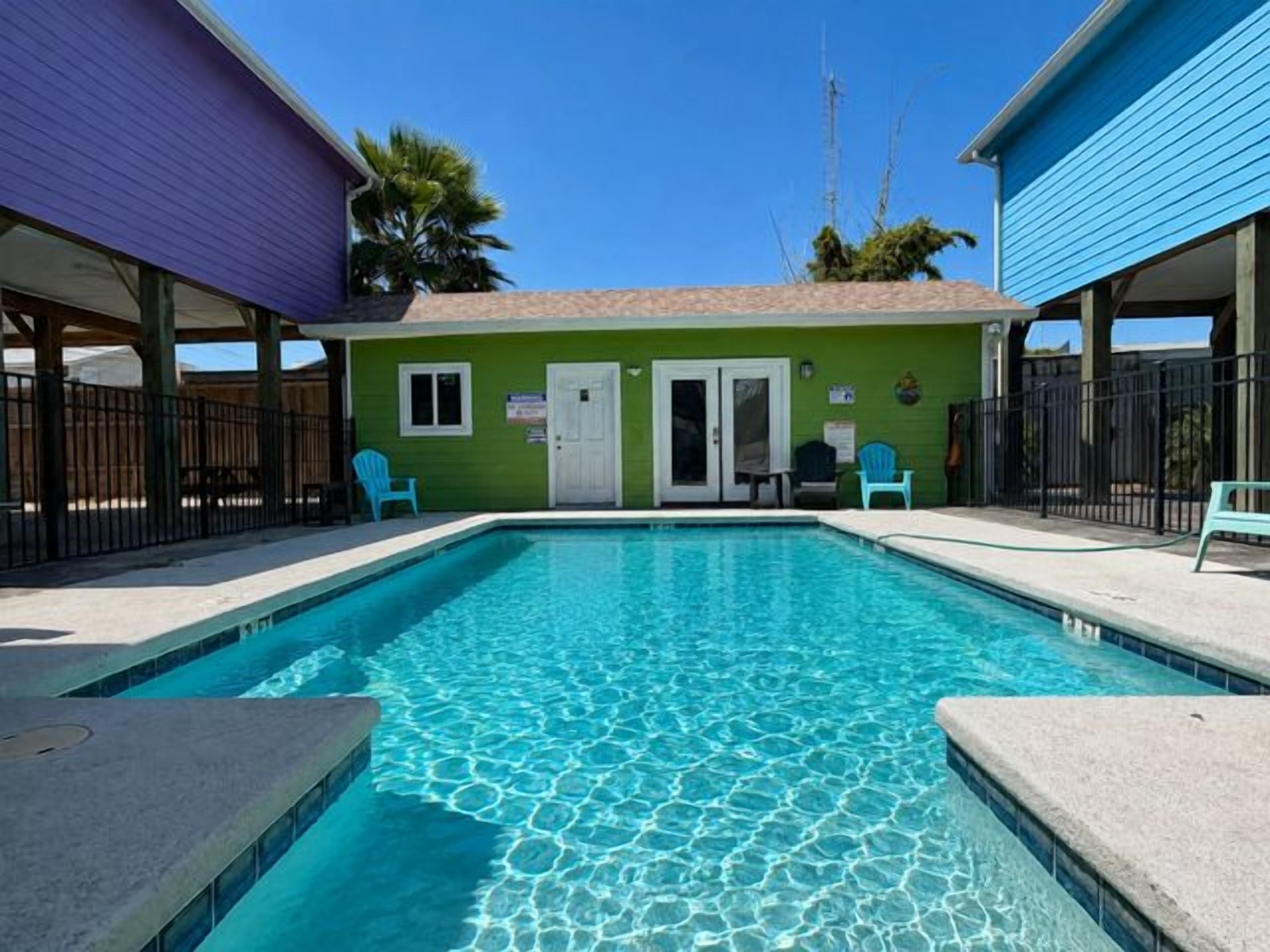 A swimming pool with a clear blue water surface, surrounded by a building with a green exterior and a door.