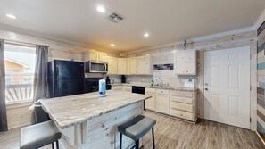 A kitchen with wooden cabinets, a black refrigerator, a microwave, a sink, and a bar area with stools. - ACC8 Shared Pool, Pet Friendly, In Town (Port Aransas)