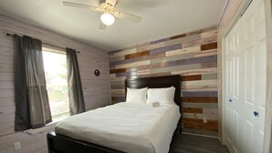 A bedroom with a bed, a ceiling fan, a window with curtains, and a wooden wall panel. - ACC9 Shared Pool, Pet Friendly, In Town (Port Aransas)