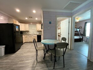A kitchen with wooden cabinets, a black refrigerator, a dining table with chairs, and a ceiling fan. - ACC9 Shared Pool, Pet Friendly, In Town (Port Aransas)