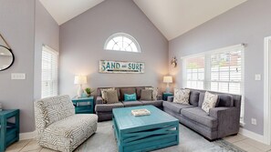 A living room with a high ceiling, a large window, a sofa set, a coffee table, and a wall sign. - FH6, Near Beach, Shared Pool, Pet Friendly, Charcoal Grill (Port Aransas)