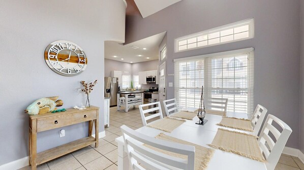 A dining area with a white table and chairs, a wooden sideboard, and a wall clock. - FH6, Near Beach, Shared Pool, Pet Friendly, Charcoal Grill (Port Aransas)