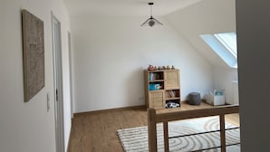 Ein Zimmer mit schrägem Dach, einem Holzregal, einem kleinen Tisch und einem Fenster.