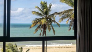 Une vue depuis une fenêtre sur une plage bordée de palmiers et donnant sur l’océan.