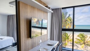 Une chambre d’hôtel dotée d’un coin repas, d’un téléviseur fixé au mur et d’une grande fenêtre donnant sur la plage.