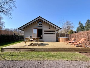 Eine kleine Holzhütte mit einer Terrasse, einem Picknicktisch und Liegestühlen.