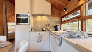 A compact kitchen with white cabinets, a built-in oven, a coffee maker, and a window overlooking a wooden deck. - Peace, Comfort & Nature at This Home (Durbuy)