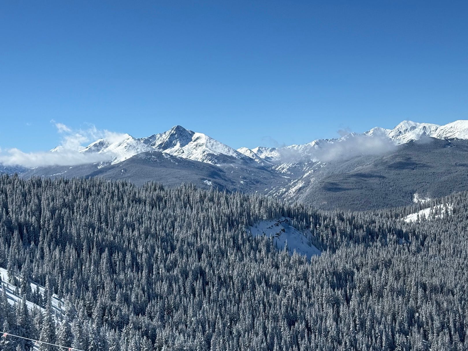 A mountainous landscape with snow-covered peaks and dense forest.