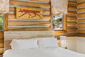 Ein schlicht eingerichtetes Schlafzimmer im Chalet-Stil mit einem Bett, einem Wandbild und einem Fenster mit Vorhängen.