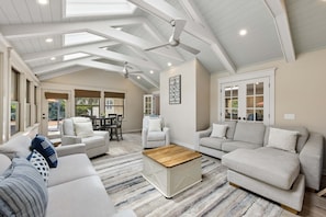 Ein geräumiges Wohnzimmer mit hohen Decken, Deckenventilatoren und großen Fenstern.