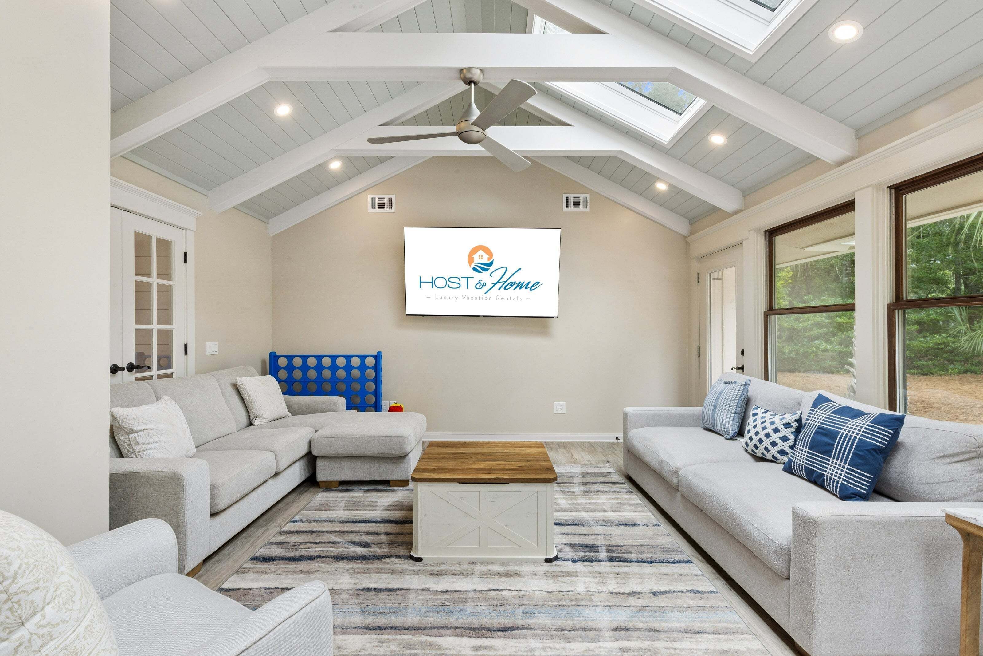 A spacious living room with a high ceiling, a ceiling fan, and a large window providing a view of the outdoors.