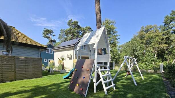 A backyard with a playhouse, a slide, and a swing set. - Comfortable Houses With Terraces (Rewal)