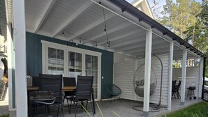 A covered patio with a table and chairs, a hanging chair, and a grill area. - Comfortable Houses With Terraces (Rewal)