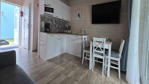 A compact kitchen with white cabinets, a microwave, and a dining area with white chairs. - Comfortable Houses With Terraces (Rewal)