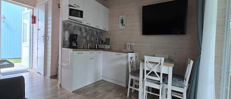 A compact kitchen with white cabinets, a microwave, and a dining area with white chairs.