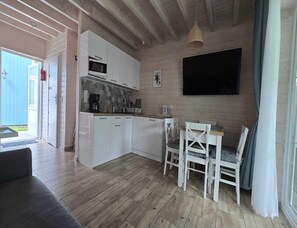 A compact kitchen with white cabinets, a microwave, and a dining area with white chairs. - Comfortable Houses With Terraces (Rewal)