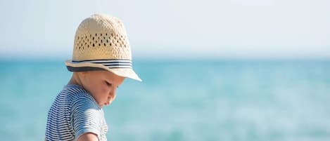 A child playing with toys on a sandy beach with the ocean in the background.