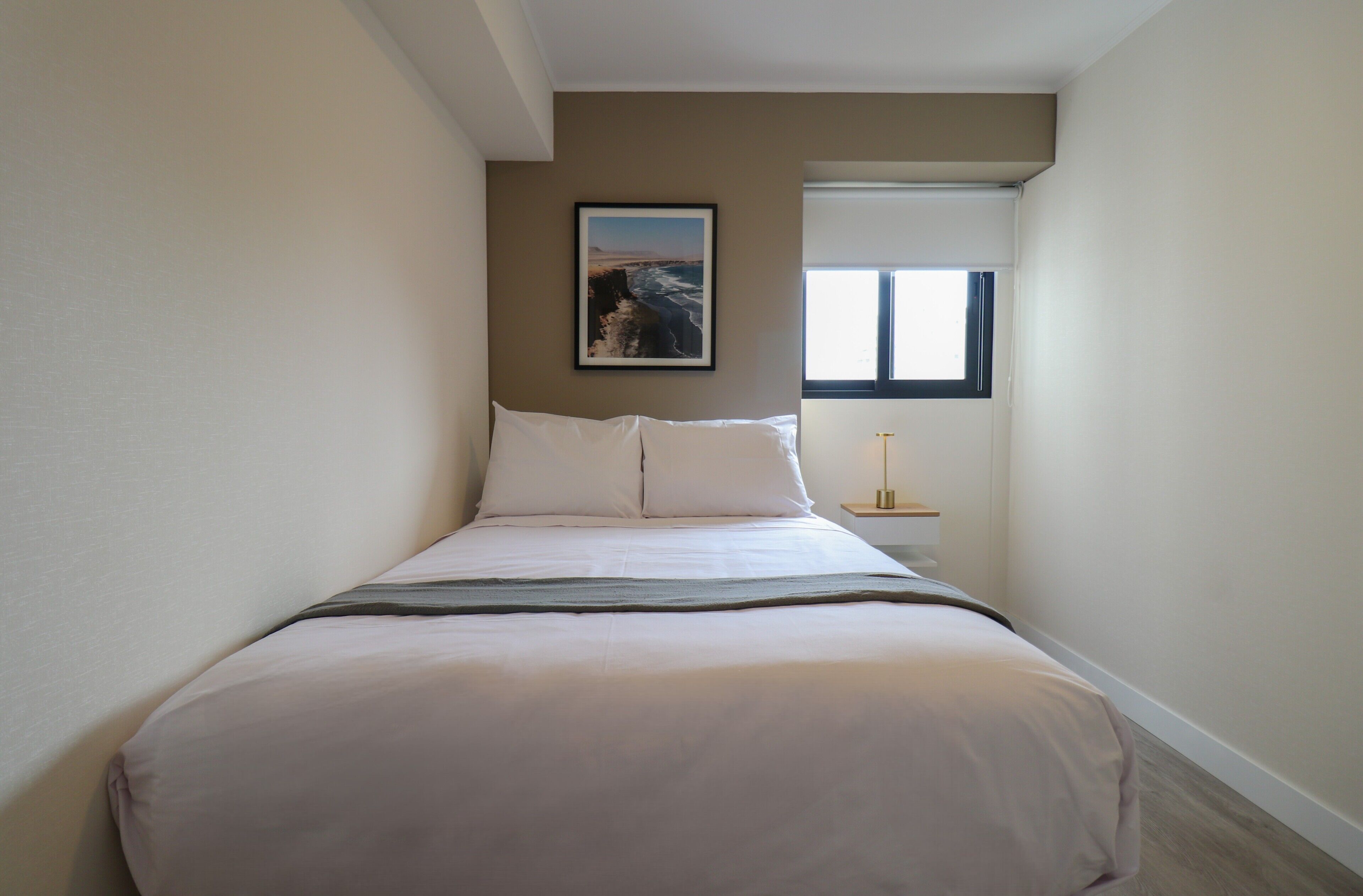 A bedroom with a bed, a nightstand, a window, and a painting on the wall.