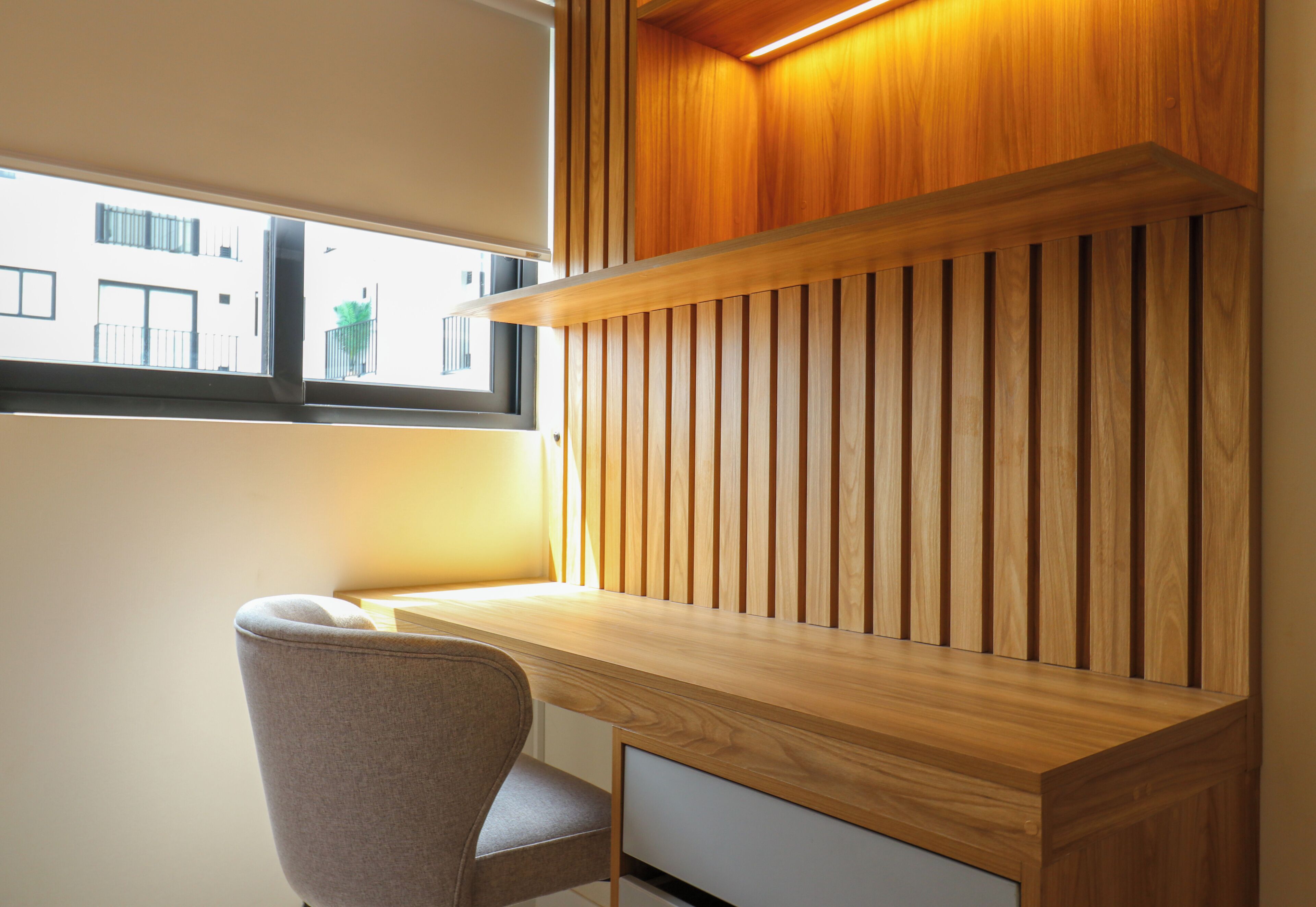 A modern desk with a wooden finish, a chair, and a window with a view of buildings.