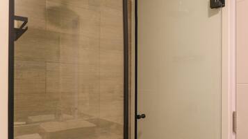 A glass-enclosed shower area with a handheld showerhead, a toilet, and a glass door.