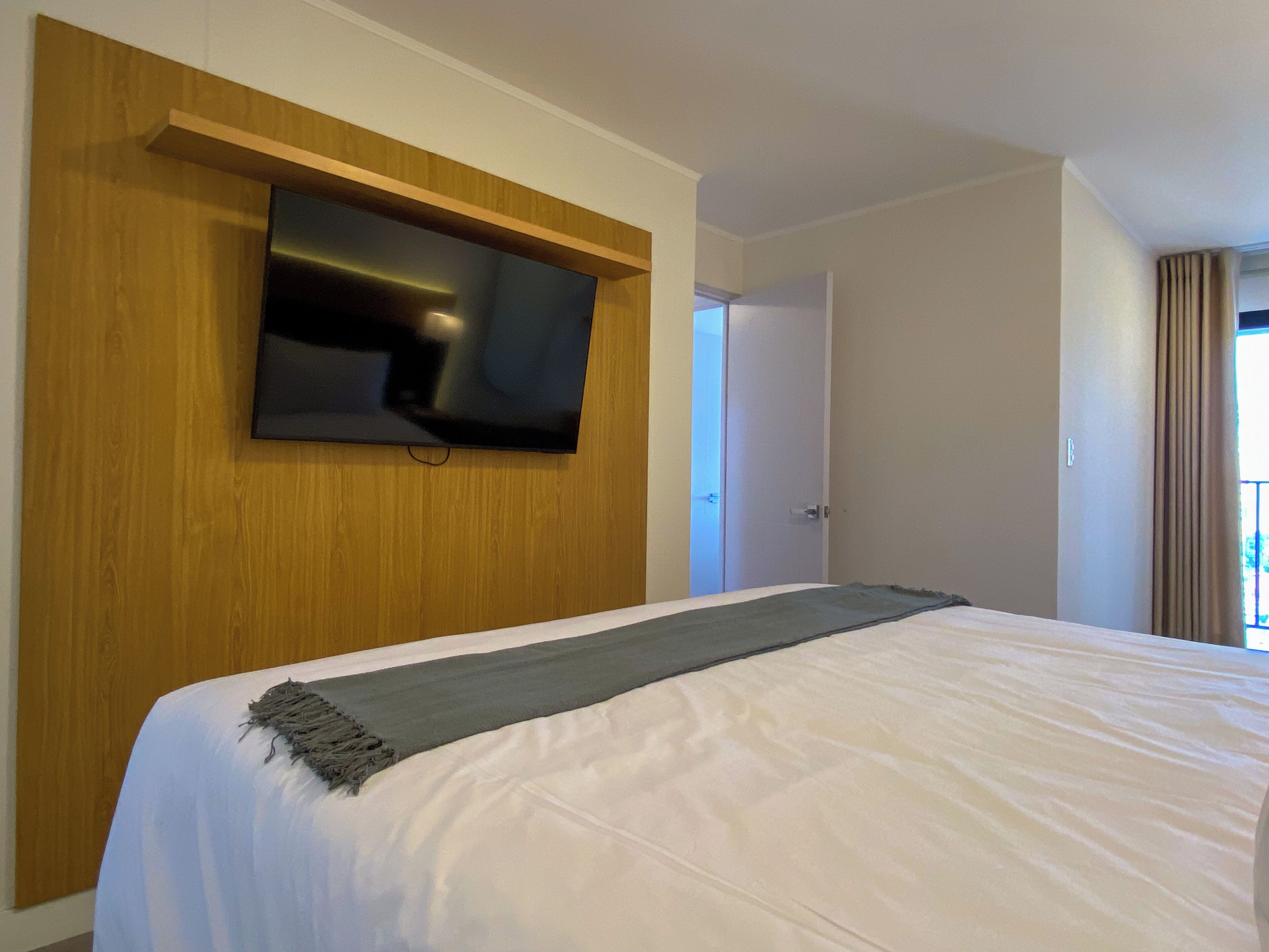 Ein Hotelzimmer mit Bett, einem Wandfernseher, einer Tür und Blick ins Freie.