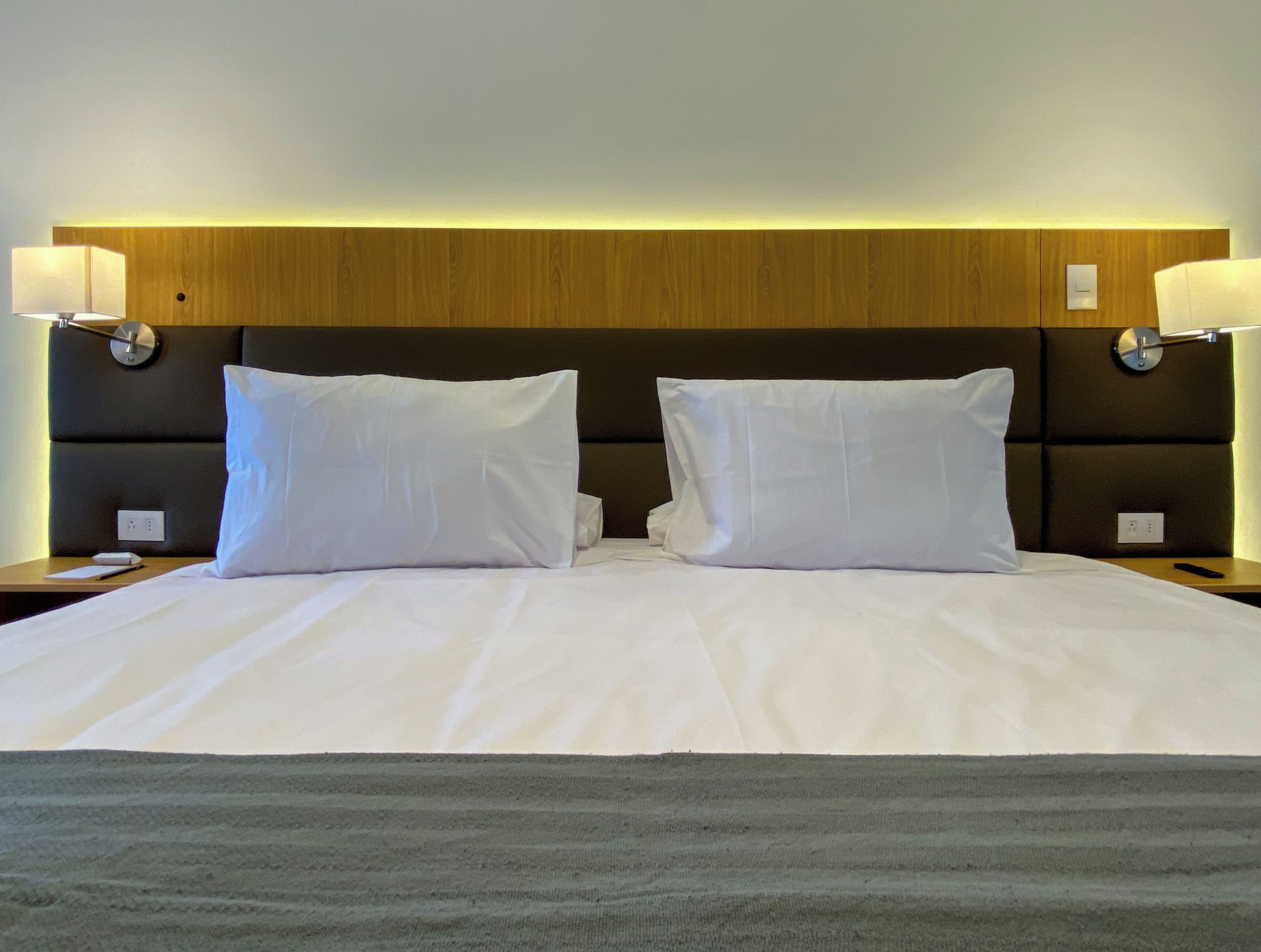 A hotel room with a large bed, two bedside lamps, and a wooden headboard.
