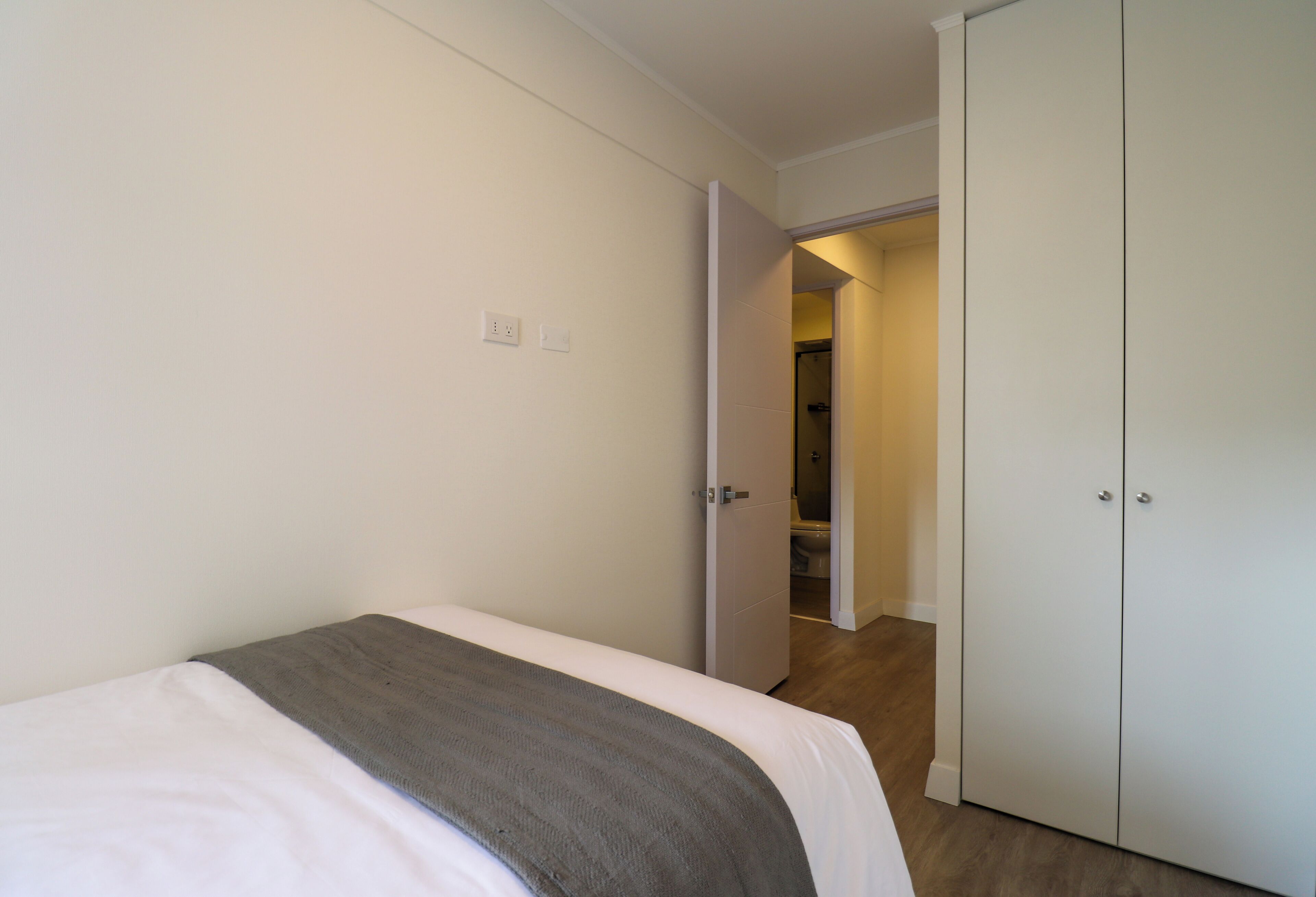 A bedroom with a bed, a wardrobe, and an open door leading to a bathroom.