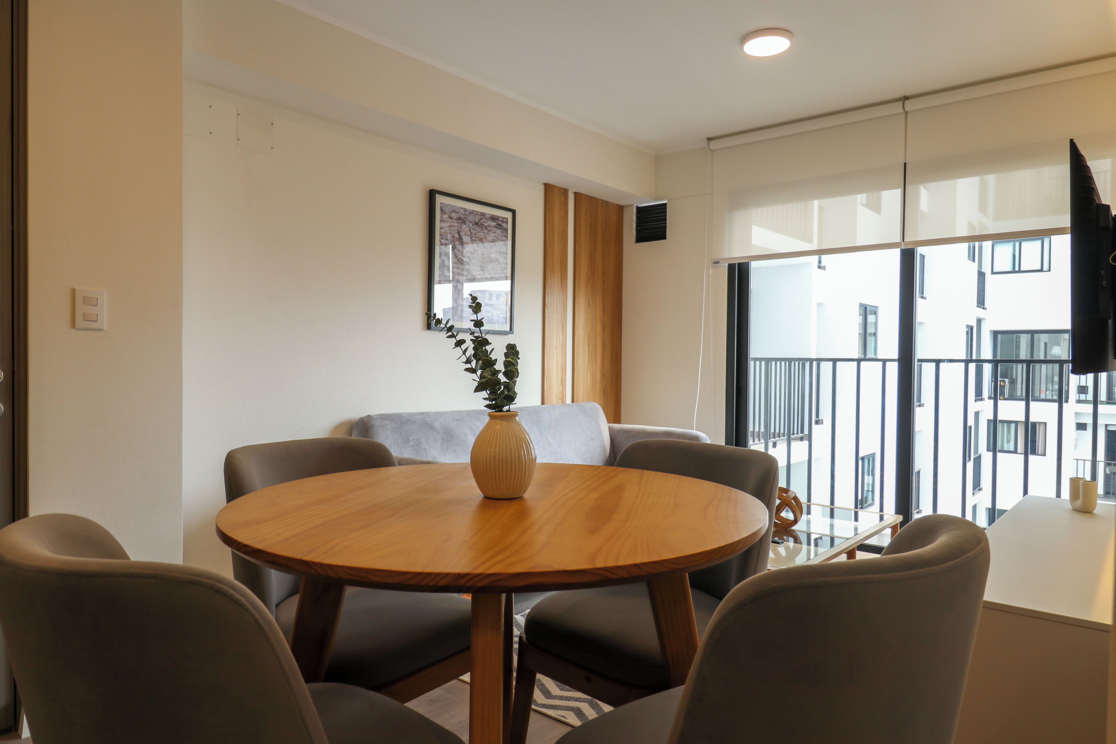 A modern living room with a round wooden table, grey sofas, and a potted plant.