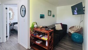 Uma sala de estar com uma mesa de centro de madeira, um sofá preto, uma bola de exercícios azul e uma televisão fixada na parede.