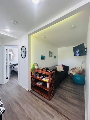 Una sala de estar con una mesa de centro de madera, un sofá negro, una pelota de ejercicios azul y un televisor montado en la pared.