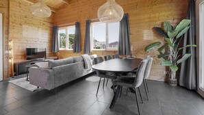 Un interior moderno con techo de madera, una zona de comedor con una mesa redonda y sillas, un sofá gris y una planta grande.