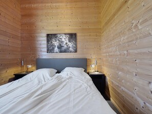 A bedroom with a wooden paneled wall, a bed with white bedding, two bedside tables with lamps, and a painting above the bed. - Country Holiday Home With Shared Pool (Someren)