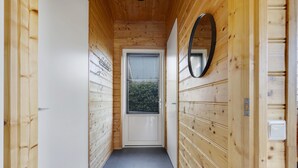 Un pasillo con paredes de madera, una puerta con ventanal y un espejo en la pared derecha.